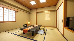 Um quarto japonês tradicional com tatames, uma mesa baixa, televisão e portas deslizantes.