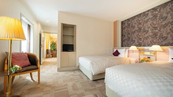 A hotel room with two beds, a television, a desk with a chair, and a large floral-patterned wall.