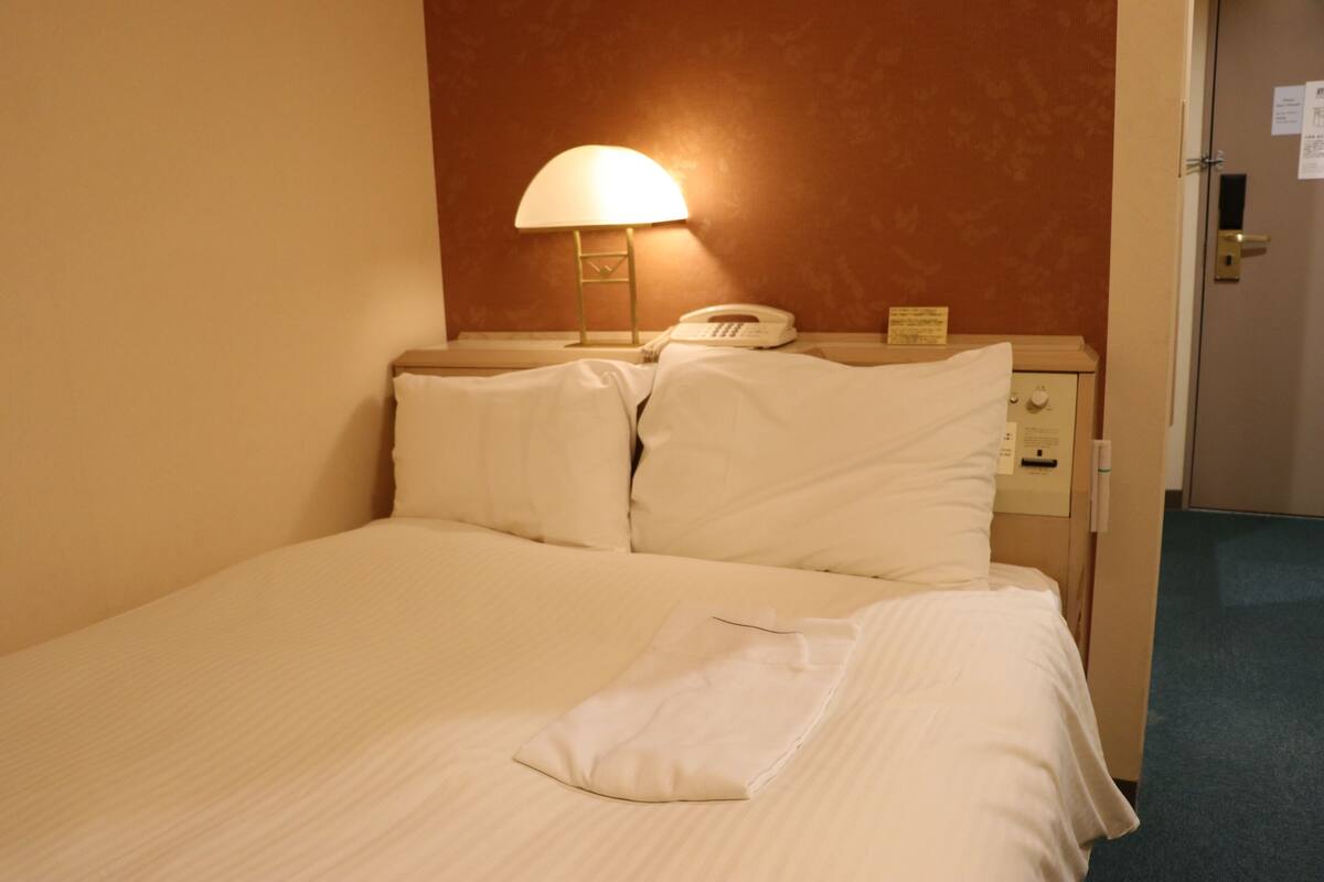A hotel room with a bed, a nightstand with a lamp, a phone, and a small cabinet.