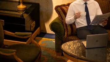 A person sitting on a sofa with a laptop and reading a newspaper.