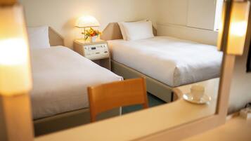 A hotel room with two beds, a bedside table with a lamp and flowers, and a chair.