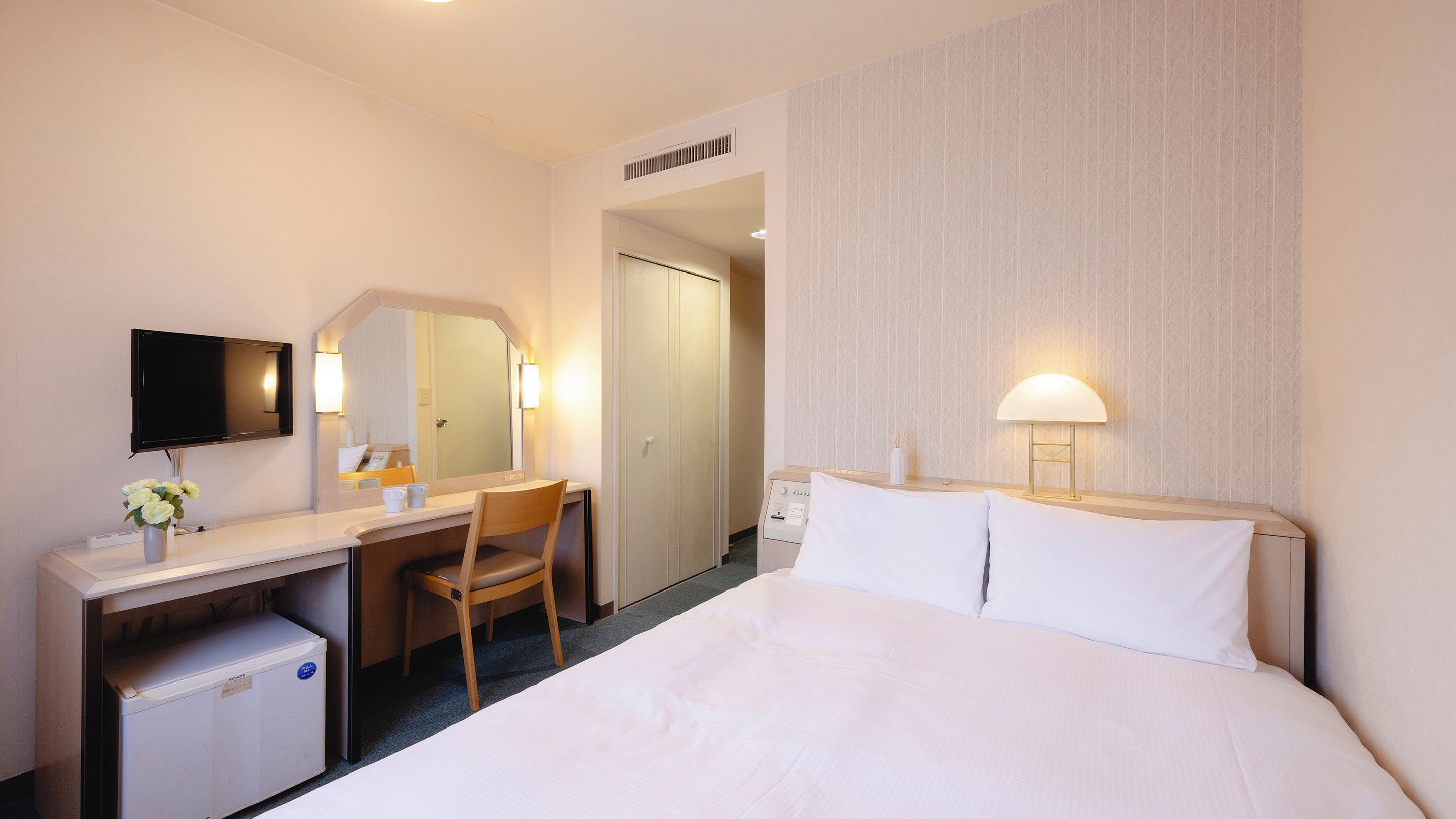 A hotel room with a bed, a desk, a chair, a television, and a bathroom door.
