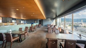 A modern restaurant with a high ceiling, large windows, and a view of a cityscape.