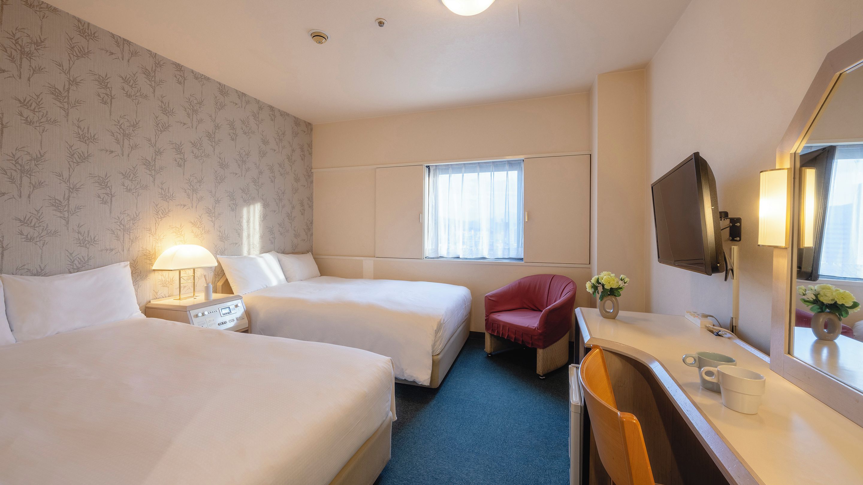 Une chambre d’hôtel avec deux lits, un bureau avec une chaise, une télévision et une fenêtre avec des rideaux.