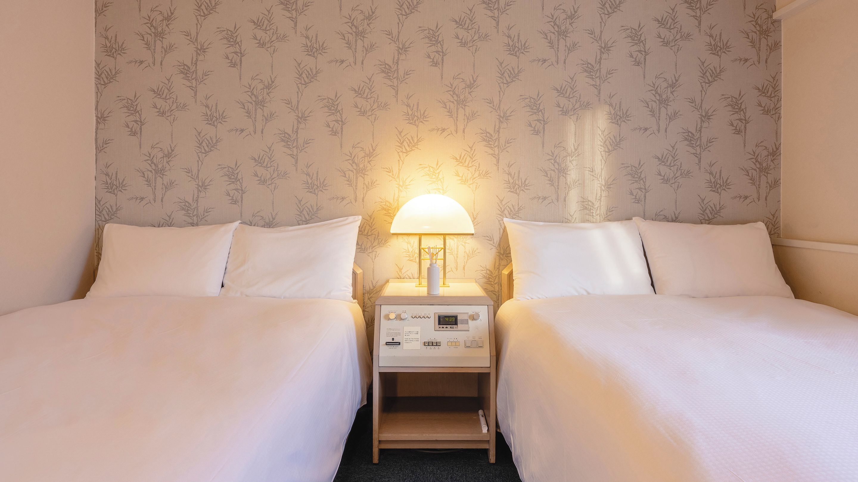 A hotel room with two beds, a bedside table with a lamp, and a wall with a bamboo pattern.