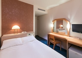 A hotel room with a bed, desk, chair, TV, and a phone.