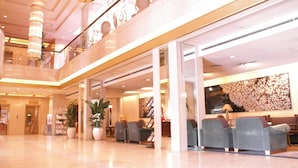 A spacious lobby with a high ceiling, a seating area with grey armchairs, and a large decorative wall. - Aizuwakamatsu Washington Hotel (Aizuwakamatsu)