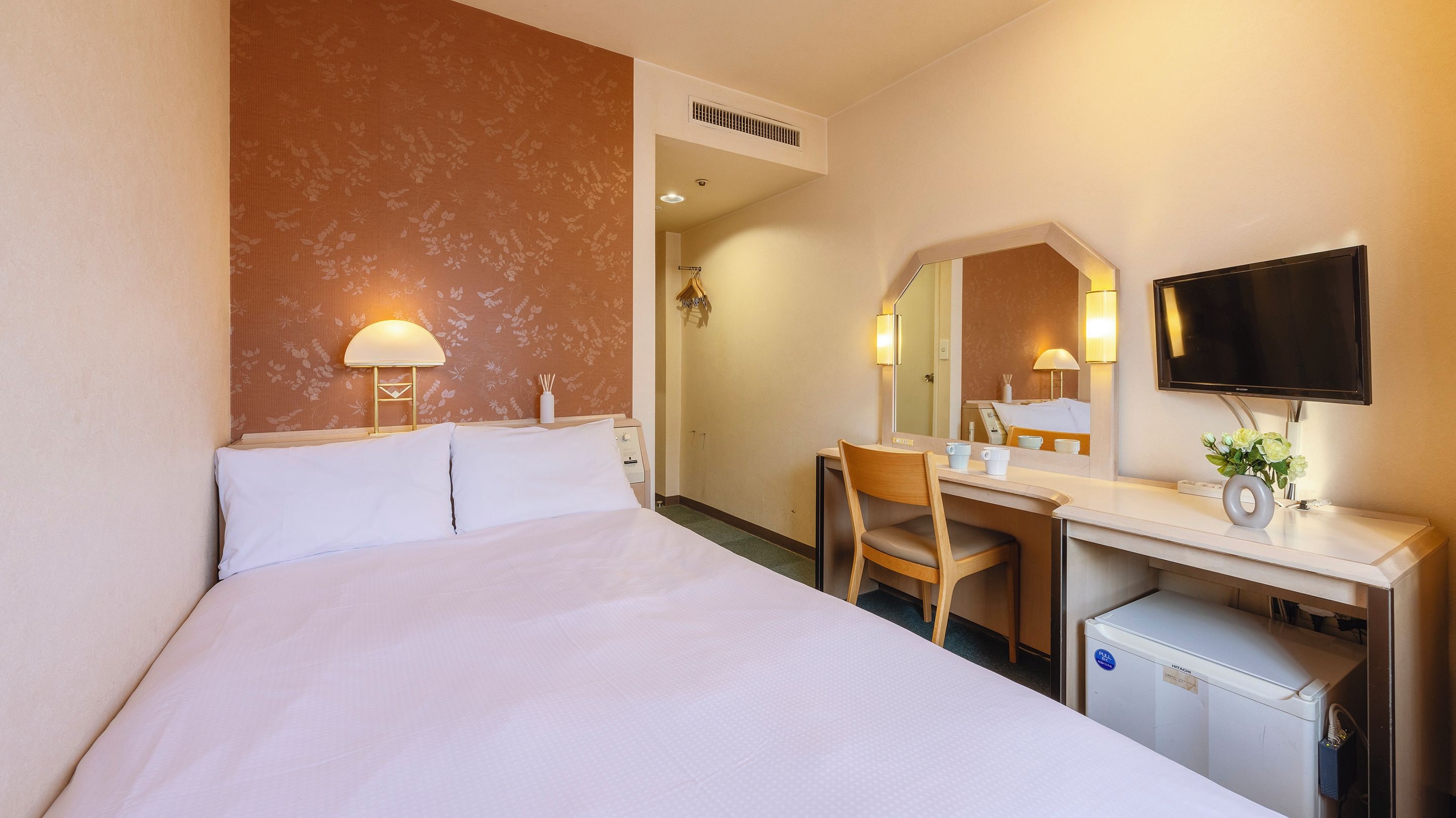 A hotel room with a bed, desk, chair, TV, and a small fridge.