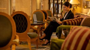 A hotel lobby with seating arrangements, a table with a laptop, and a person reading a magazine. - Aizuwakamatsu Washington Hotel (Aizuwakamatsu)
