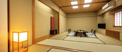 A traditional Japanese room with tatami flooring, a low table with cushions, a television, and a sliding door.