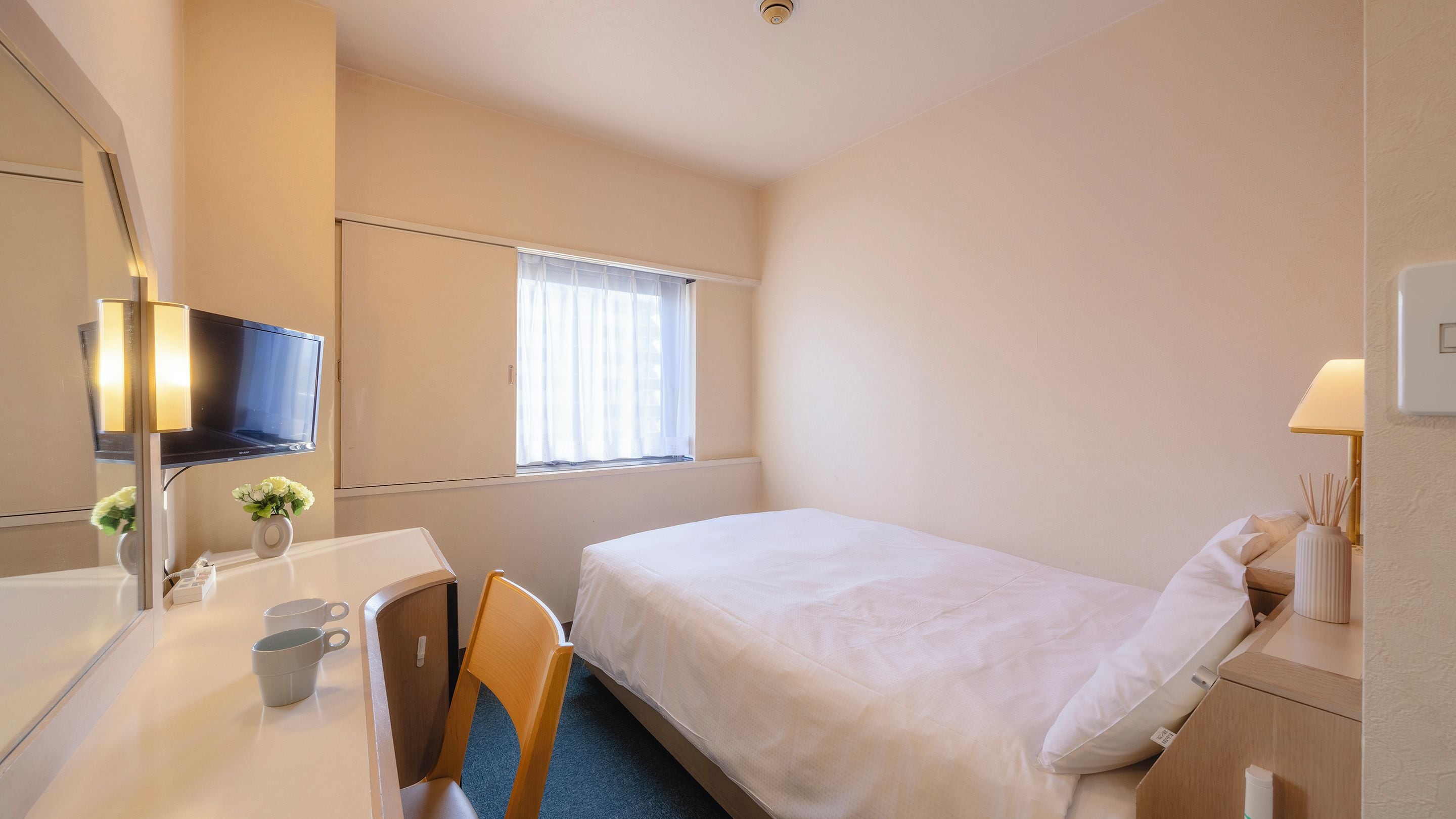 Habitación de hotel con cama, escritorio, silla, televisor y ventana con cortinas.