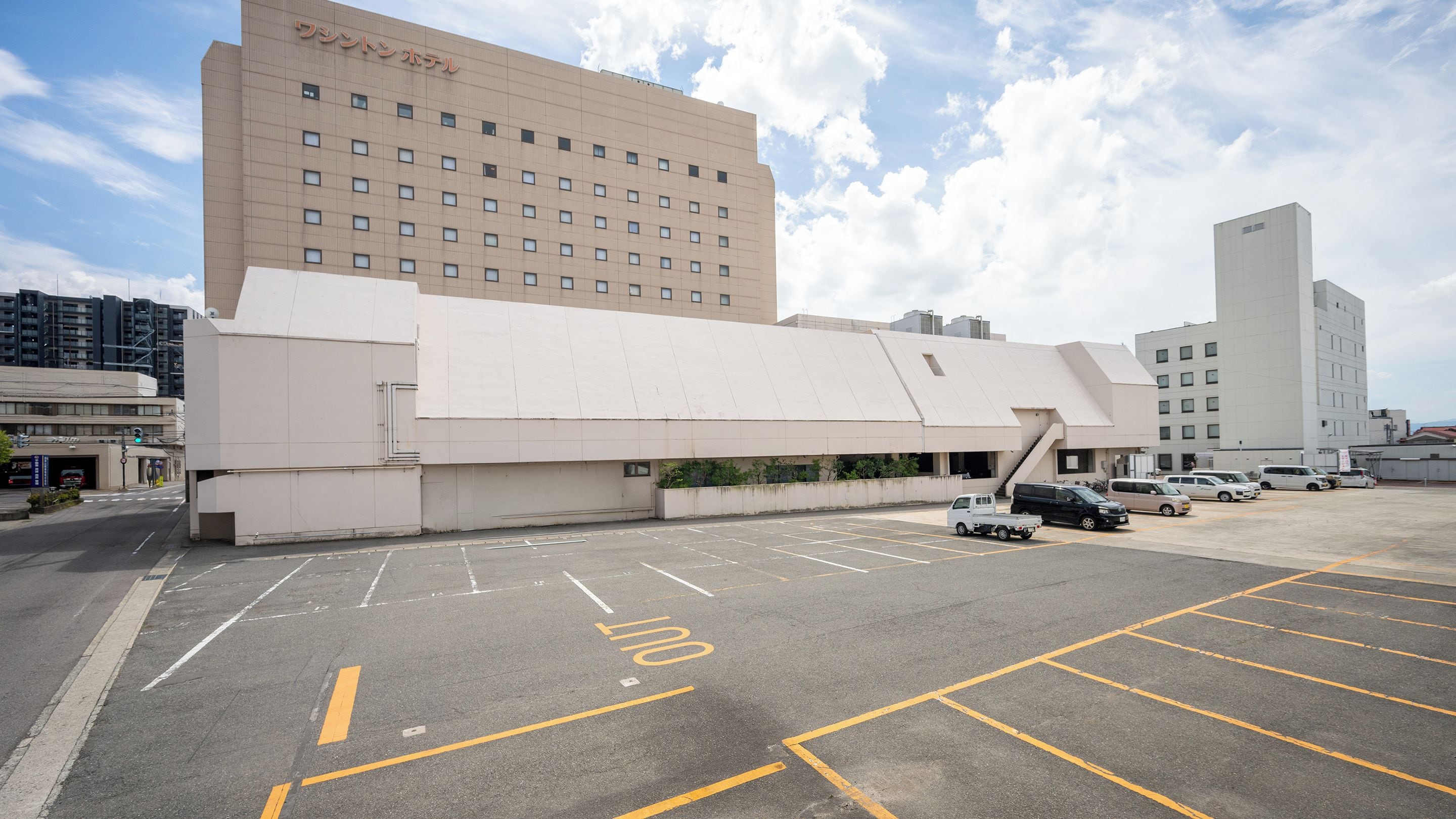 A hotel with a modern design, featuring a large parking lot and multiple vehicles.