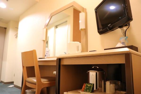 Una camera d'albergo con una scrivania in legno, una sedia, un televisore a parete e una macchina per il caffè.