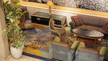 A room with a sofa, armchairs, a glass-top coffee table, a side table, a lamp, and a potted plant.