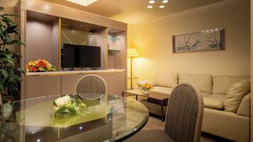 A hotel room with a round glass table, a sofa, a television, and a painting on the wall.