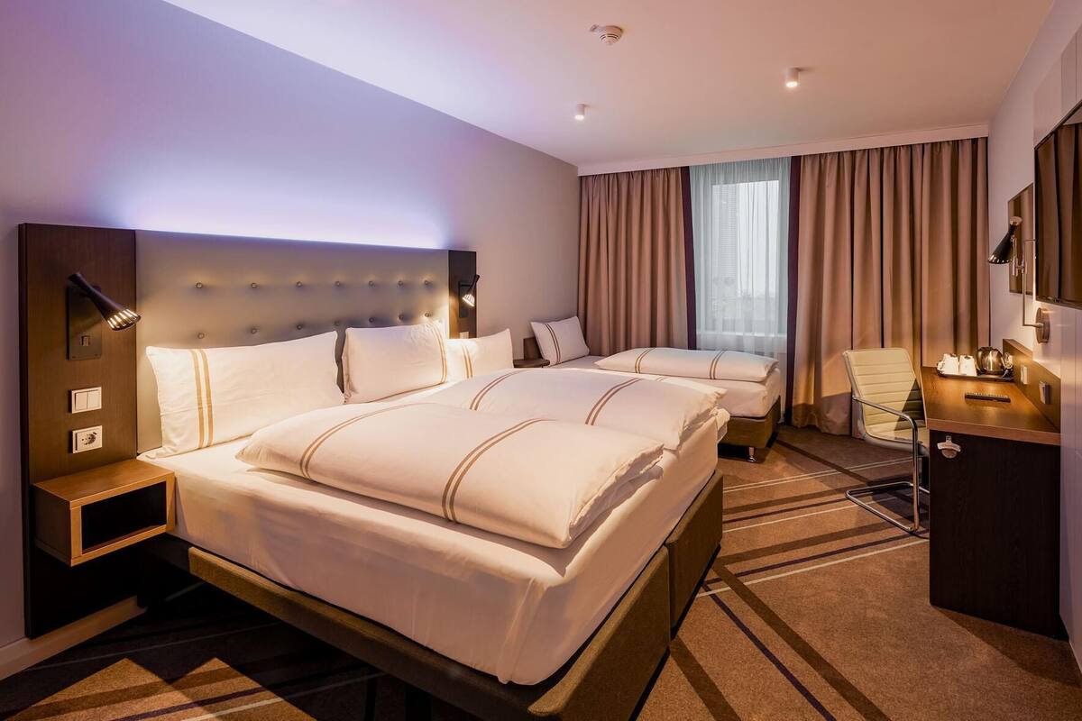 Una habitación de hotel con una cama grande, una cama más pequeña, un escritorio, una silla y un televisor.