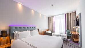 Une chambre d’hôtel avec un grand lit, un bureau, une chaise, une télévision et une fenêtre avec des rideaux.