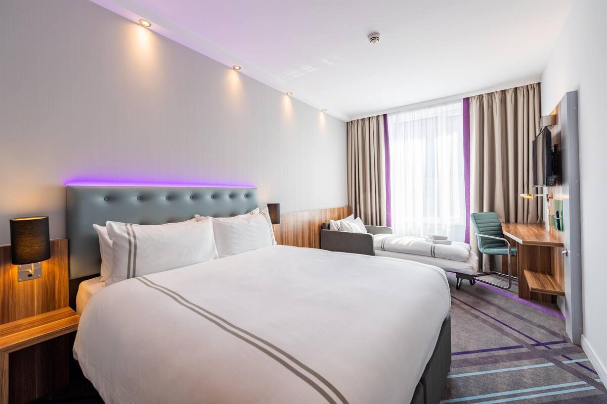 Una habitación de hotel con una cama grande, un escritorio, una silla, un televisor y una ventana con cortinas.