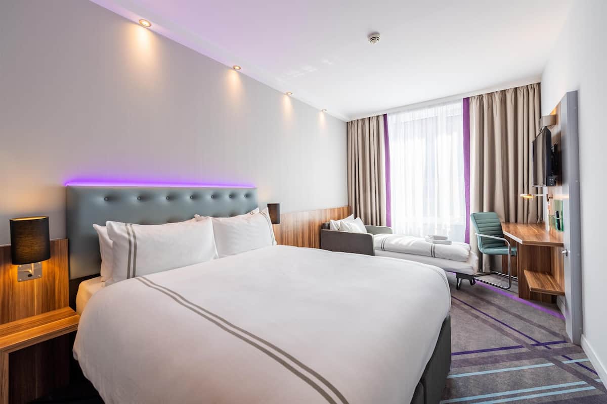 Una habitación de hotel con una cama grande, un escritorio, una silla, un televisor y una ventana con cortinas.