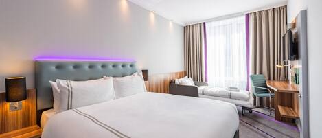 Una habitación de hotel con una cama grande, un escritorio, una silla, un televisor y una ventana con cortinas.