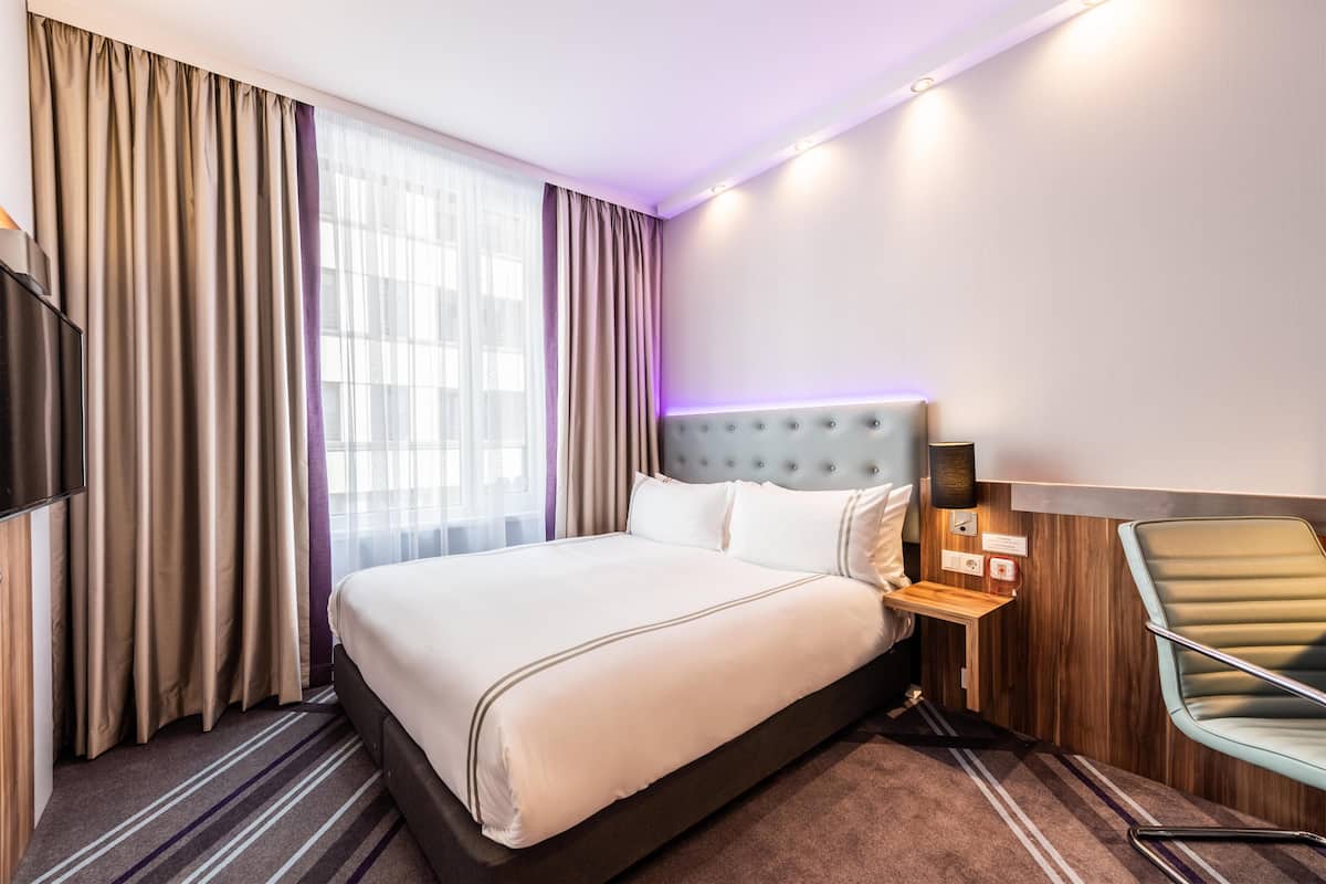 Una habitación de hotel con una cama grande, televisión, mesita de noche, lámpara y una silla.