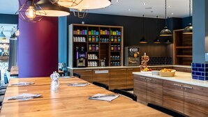 L’intérieur d’un restaurant moderne, avec des tables en bois, un espace central pour servir les plats et divers récipients contenant de la nourriture, disposés sur des étagères.