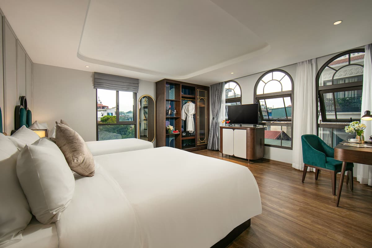 Une chambre d’hôtel avec un grand lit, un bureau avec une télévision et une vue sur la ville grâce à de grandes fenêtres.