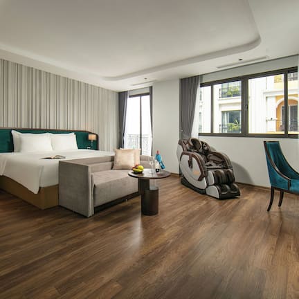 A modern hotel room with a large bed, a sitting area with a coffee table, a treadmill, and a dining table with chairs.