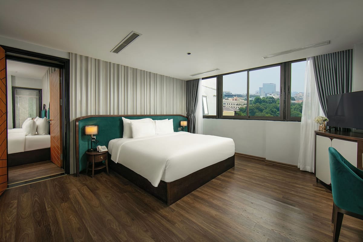 Une chambre d’hôtel avec un grand lit, un bureau avec une télévision, une chaise et une vue sur la ville grâce à de grandes fenêtres.