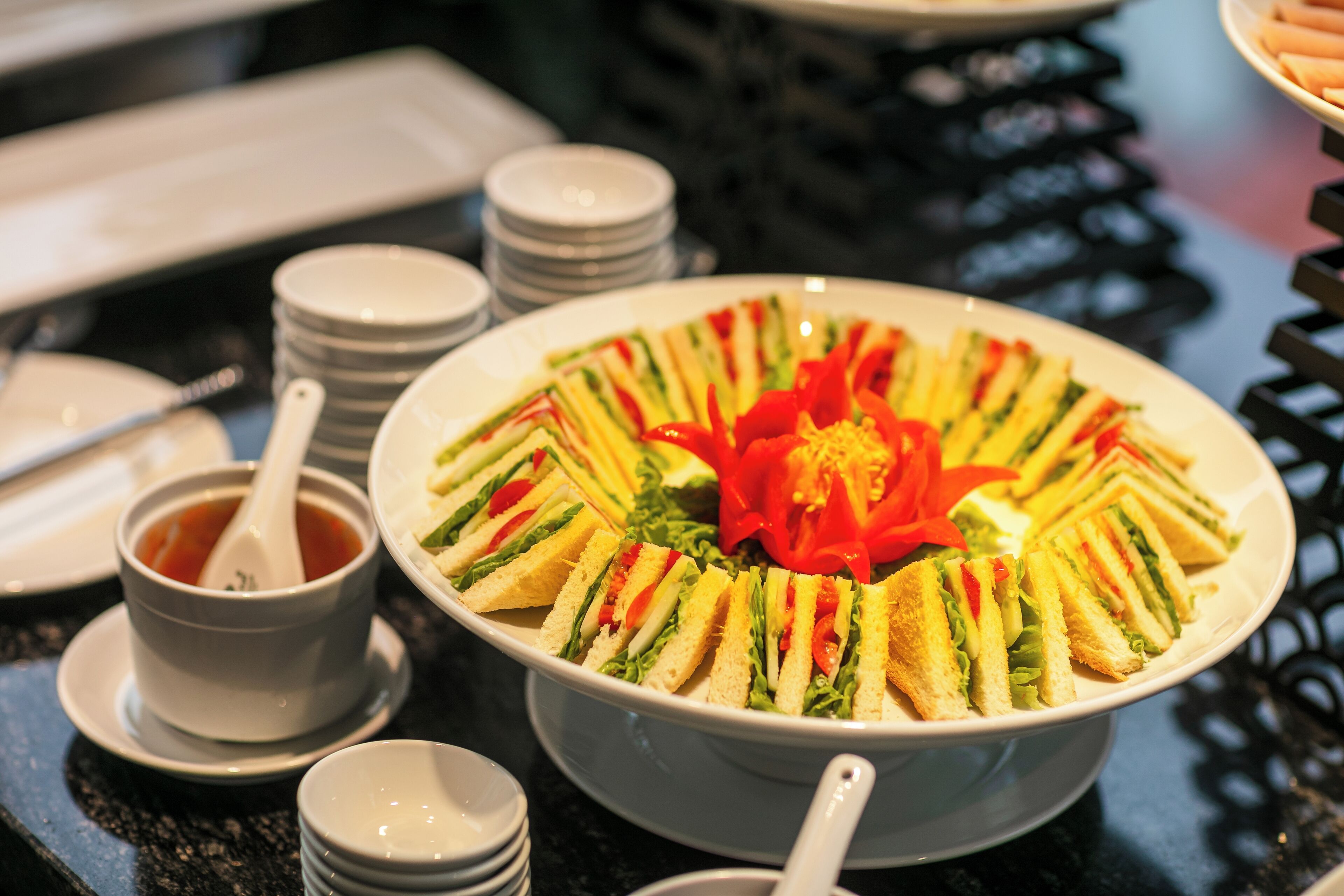 A table with a large bowl of sandwiches arranged in a circular pattern, surrounded by small bowls and spoons.