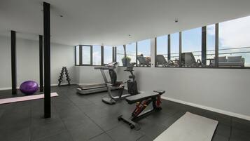 A modern gym with exercise equipment, a yoga mat, and large windows offering a view of the city.