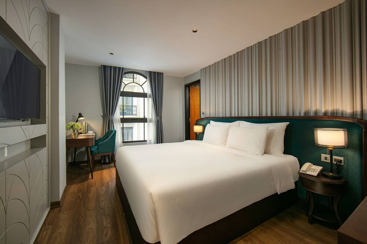 Une chambre d’hôtel avec un grand lit, un bureau avec une chaise, une télévision et une fenêtre avec des rideaux.