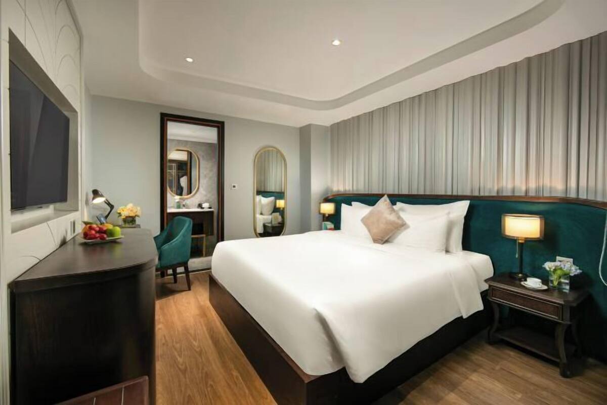 Une chambre d’hôtel avec un grand lit, un bureau avec un miroir, une chaise et une table de chevet avec une lampe.
