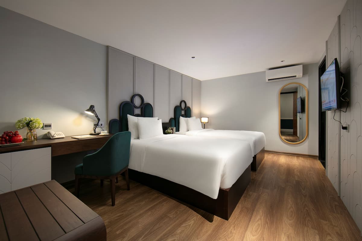 Une chambre d’hôtel moderne, dotée d’un grand lit, d’un bureau avec une lampe, d’une chaise et d’un téléviseur fixé au mur.