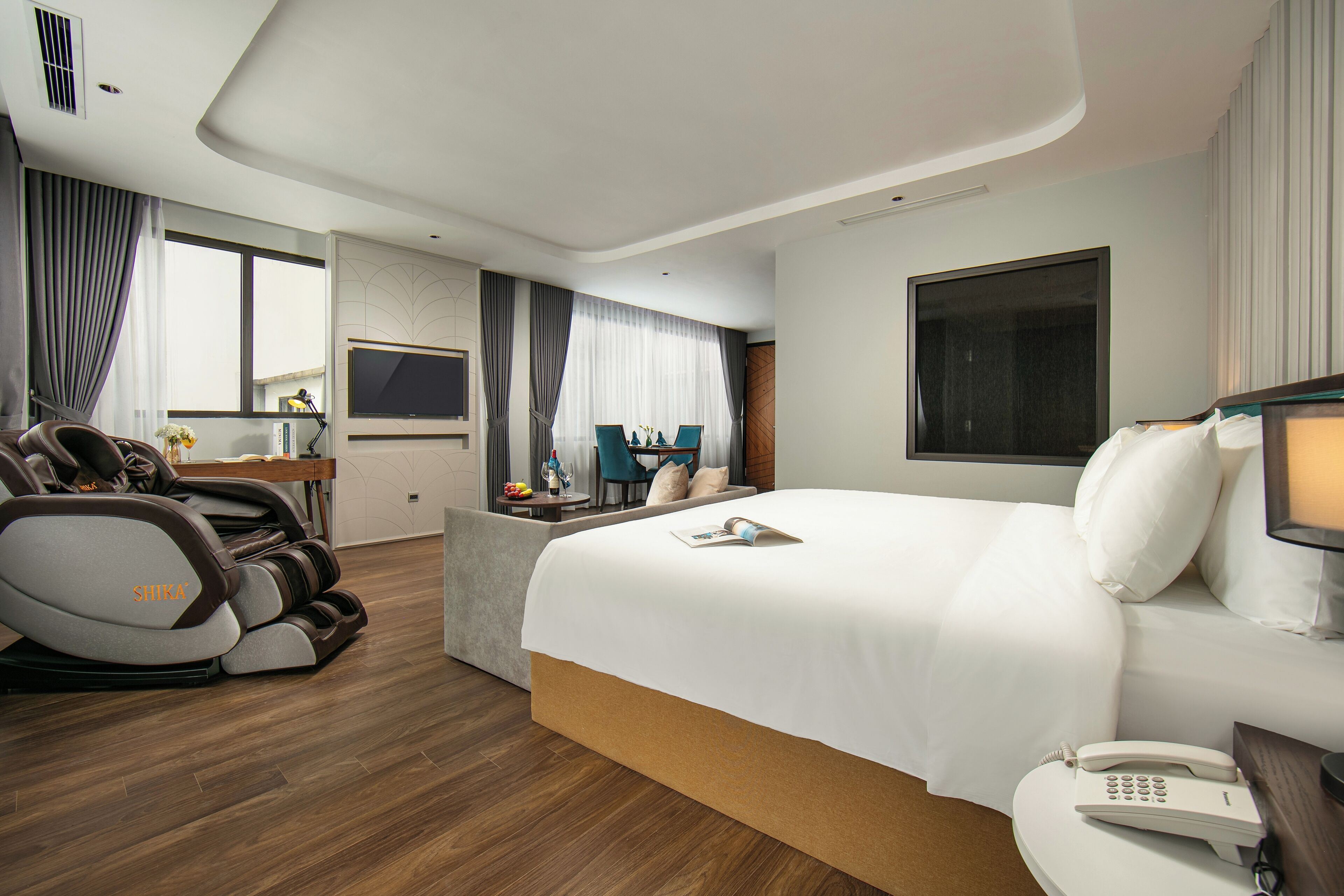 A modern hotel room with a large bed, a massage chair, a desk, and a TV.