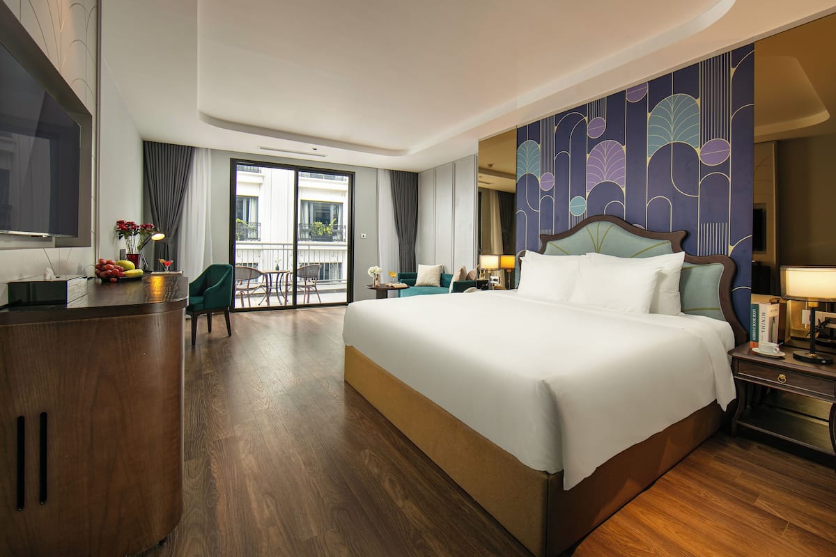 Une chambre d’hôtel avec un grand lit, un bureau doté d’une télévision à écran plat, une chaise, un balcon avec vue et un mur décoratif.