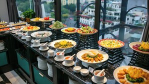 A buffet with various dishes, including salads, sushi, and appetizers, arranged on a counter with a city view in the background. - May De Ville Lakeside Hotel (Hanoi)