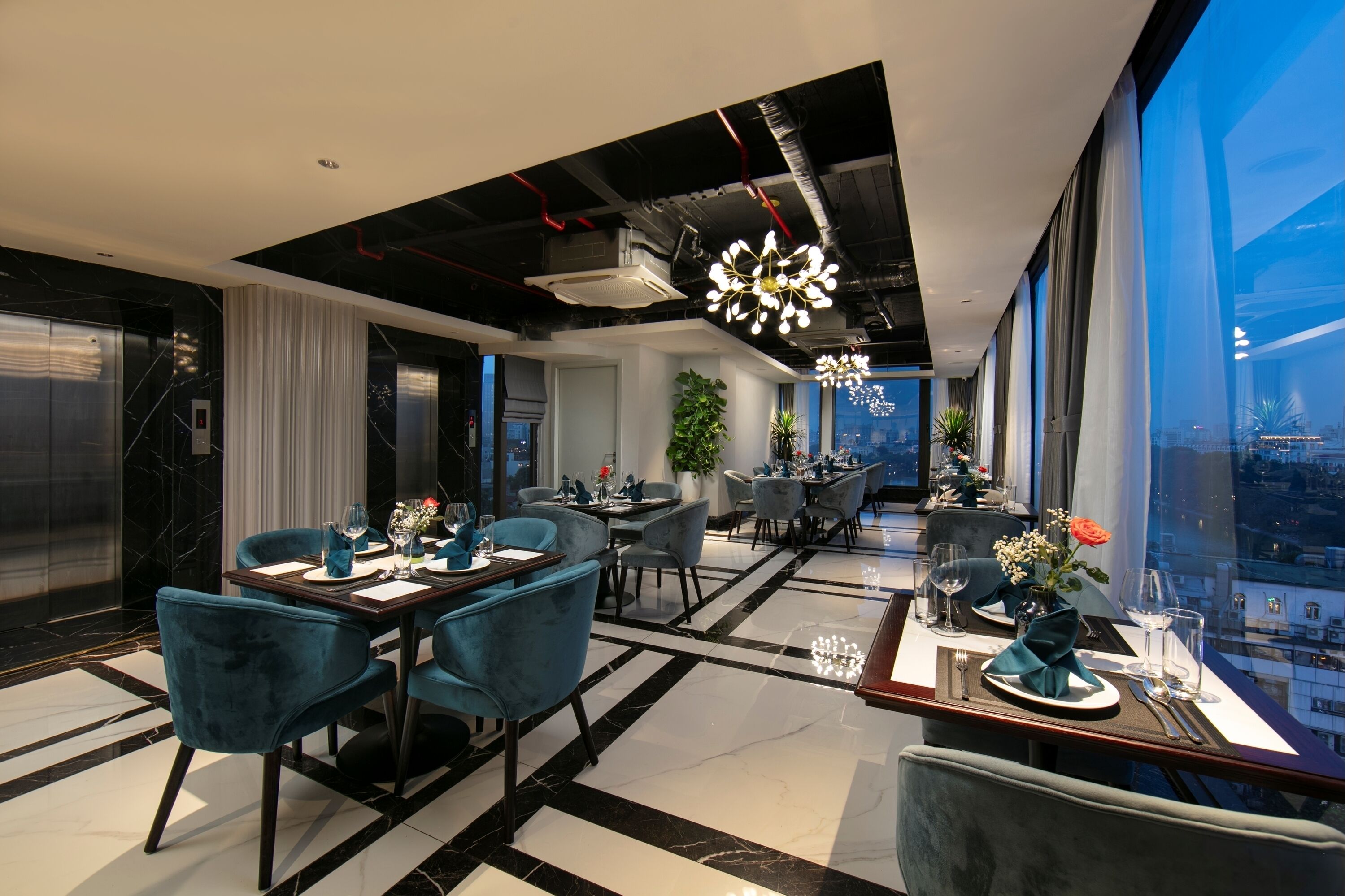 A modern dining area with a high ceiling, black and white marble flooring, and large windows offering a city view.