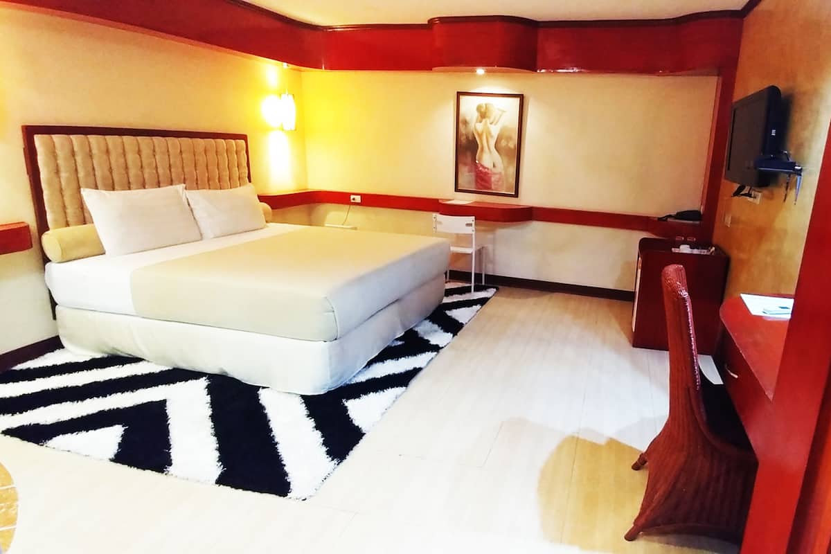 A hotel room with a bed, a desk, a chair, a television, and a painting on the wall.
