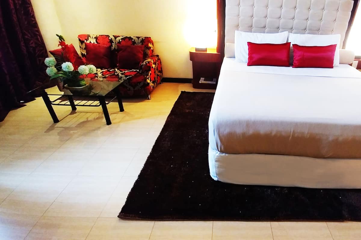 A hotel room with a bed, a nightstand, a chair, and a table with a vase of flowers.