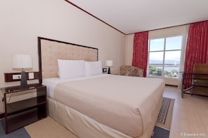A hotel room with a large bed, a nightstand, a chair, and a window with a view. - Dulcinea Hotel and Suites (Lapu-Lapu)