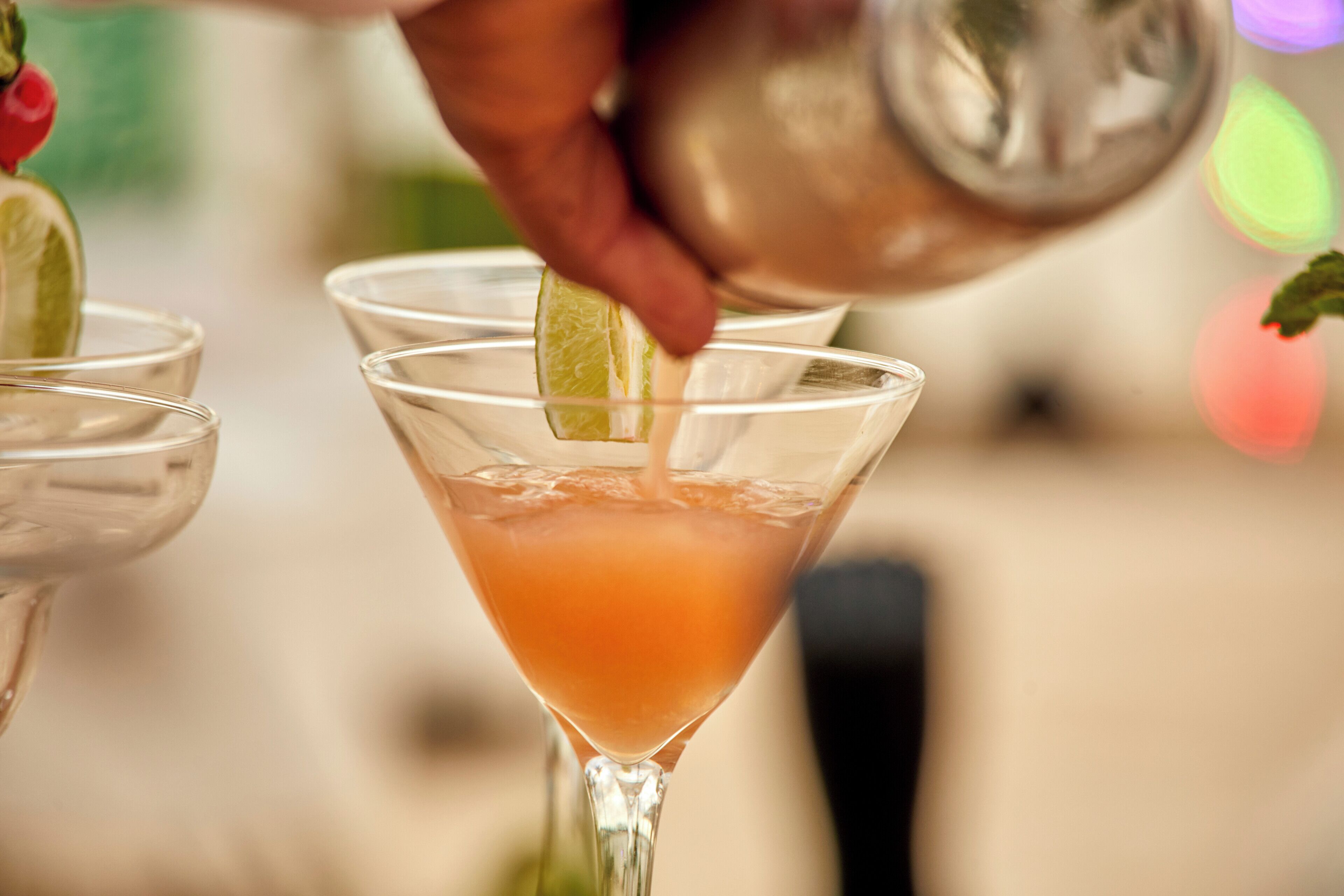 A cocktail being poured into a martini glass.