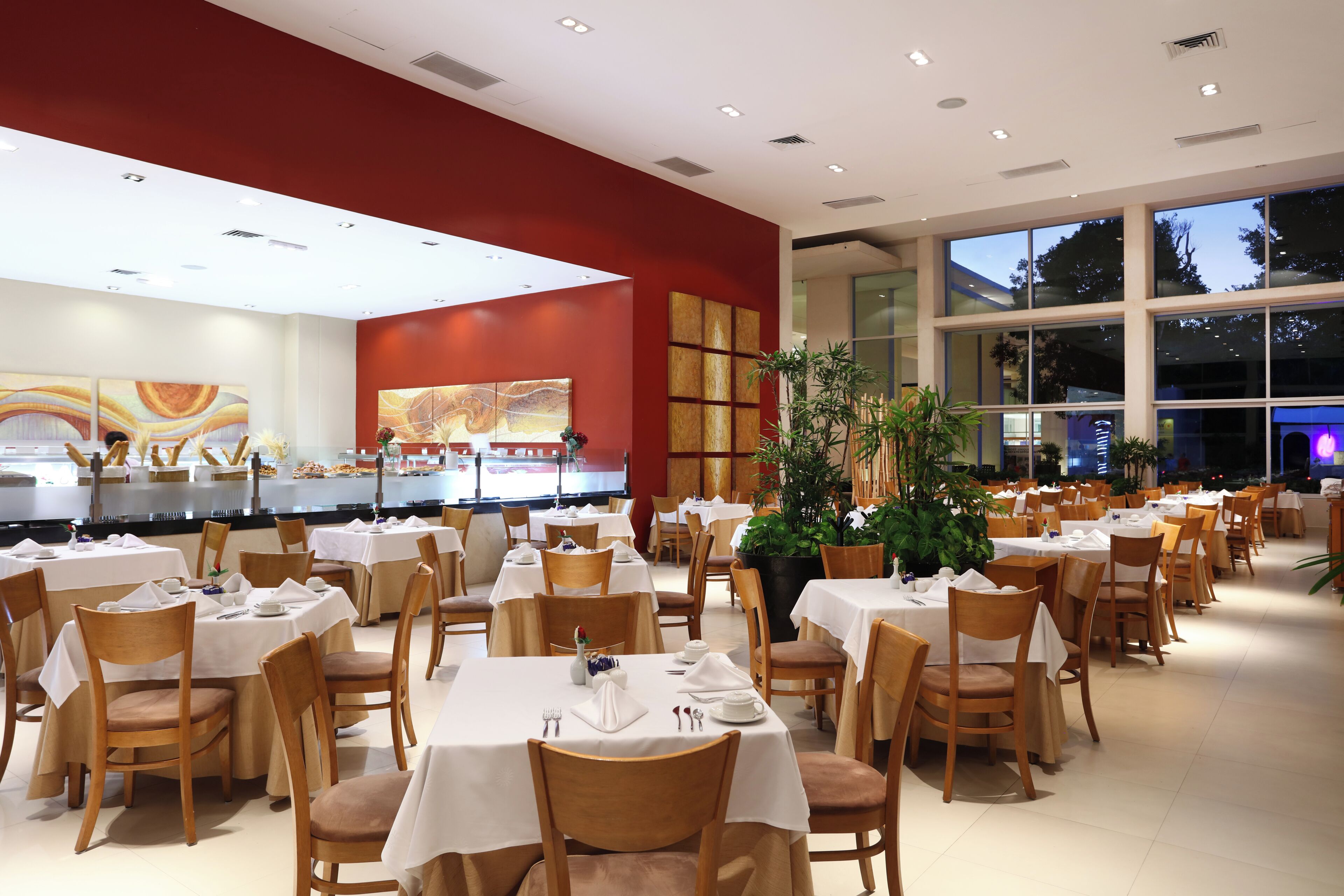 A restaurant with multiple tables and chairs, a buffet area, and large windows.