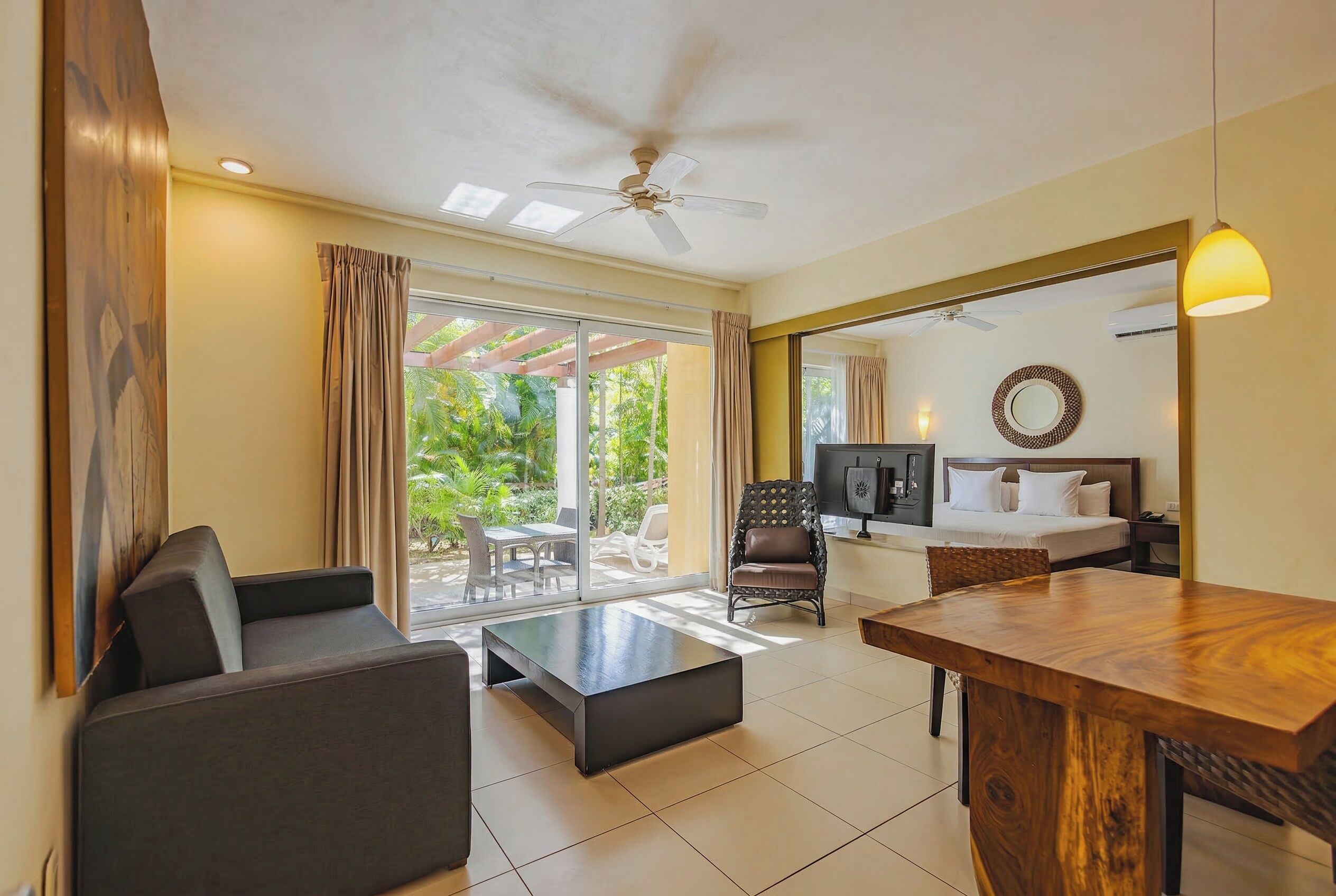 Habitación de hotel con zona de comedor, sofá, sillón, cama y vistas al exterior.