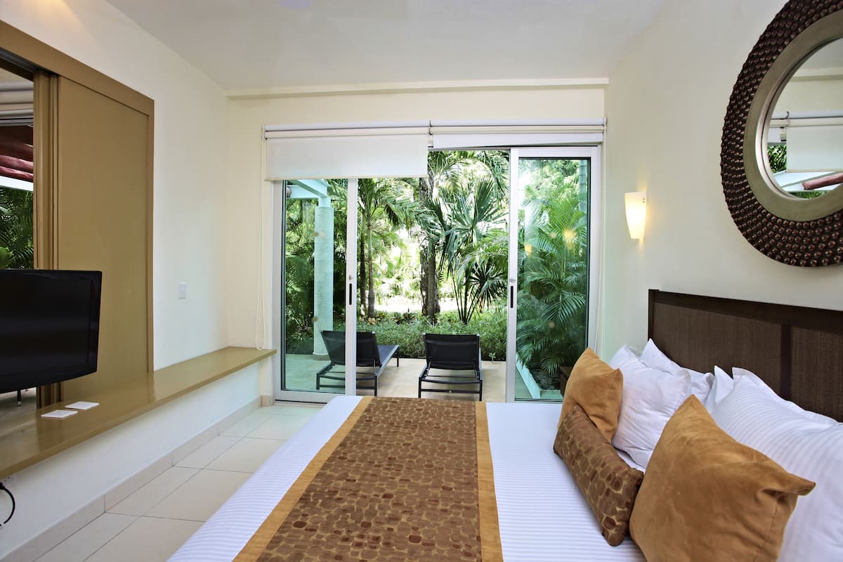 A hotel room with a bed, a TV, a desk, and a balcony with a table and chairs.