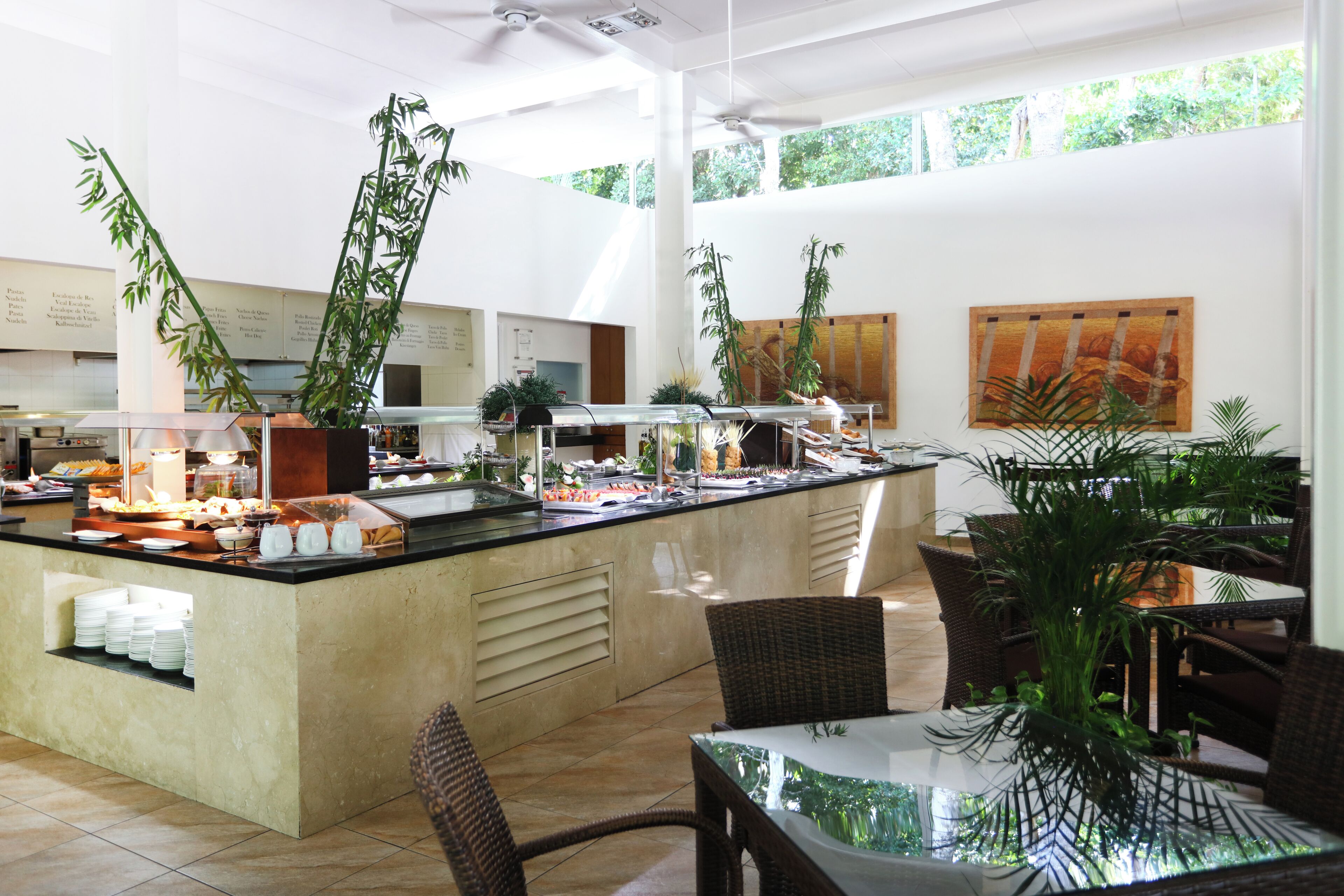 Un espace buffet proposant une variété de plats, un coin salon avec des meubles en osier et de grandes fenêtres laissant entrer la lumière naturelle.