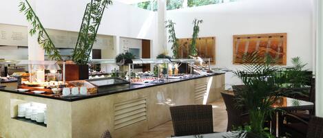 Un espace buffet proposant une variété de plats, un coin salon avec des meubles en osier et de grandes fenêtres laissant entrer la lumière naturelle.