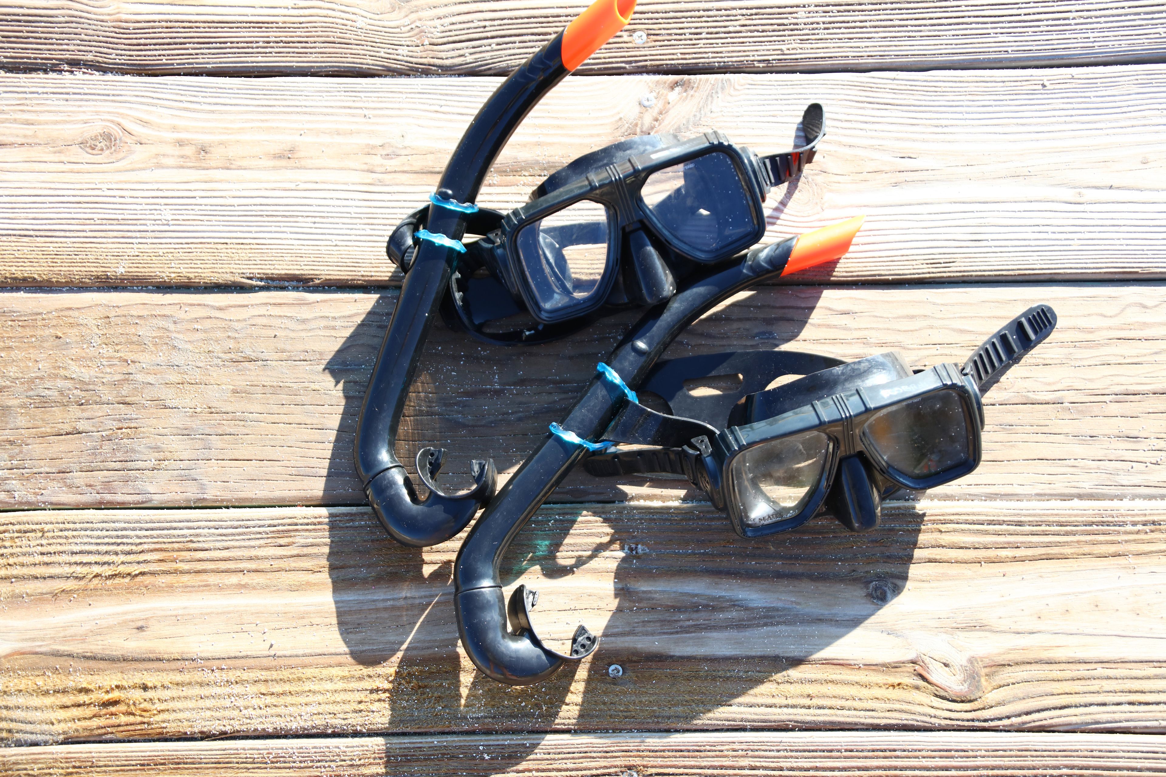 Un paio di attrezzatura da snorkeling nera e arancione con cinture blu, su una superficie di legno.