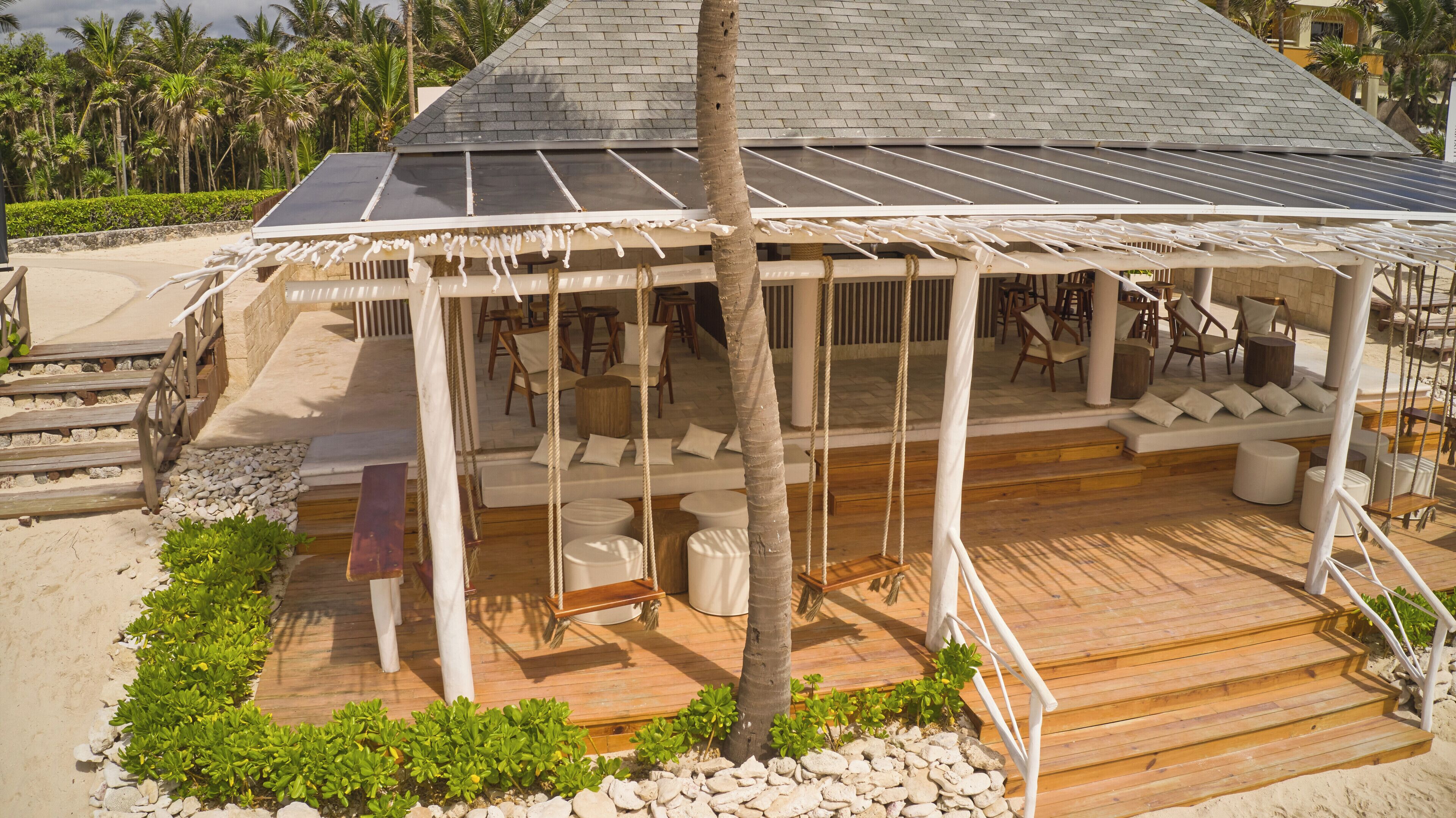 A covered outdoor seating area with a wooden deck, white cushions, and a palm tree.