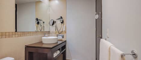 Un baño con lavamanos, espejo, secador de pelo y toallero.